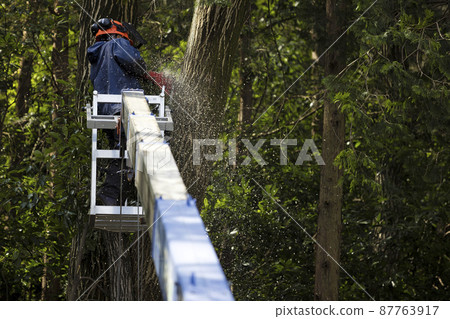 Senior man riding a crane car gondola with a chainsaw 87763917