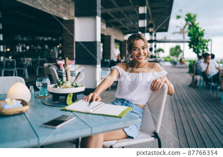 Cheerful stylish woman sitting with notebook in cozy outdoor cafe 87766354