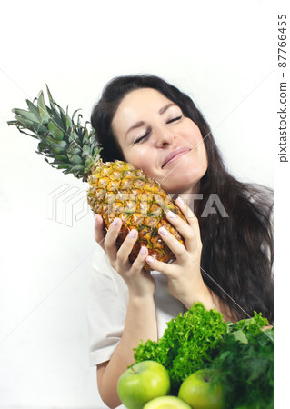 A smiling woman with vegetables and fruits. Pineapple, apples and celery. The concept of spring and vitamins. Detox food. Front view. 87766455