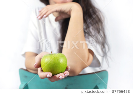 Close-up of a woman's hand holding an apple. The concept of spring and vitamins. Detox food. Front view. 87766458