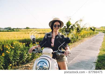 Beautiful hipster girl testing vintage moped during journey Beautiful hipster girl testing vintage moped during journey 87766475