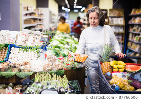 Interested aged woman choosing fresh carrots in supermarket Interested aged woman choosing fresh carrots in supermarket 87766600