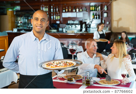 Hospitable latin american waiter welcoming guests in pizza restaurant Hospitable latin american waiter welcoming guests in pizza restaurant 87766602
