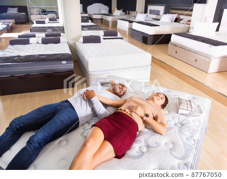 Cheerful loving Hispanic couple lying on new modern orthopedic mattress in furniture shop trying its comfort and convenience 87767050
