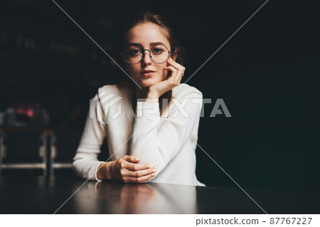 Pensive woman in eyeglasses sitting at table 87767227