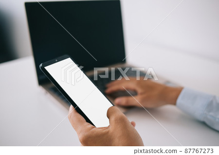 Crop man working on laptop and messaging on smartphone in office 87767273