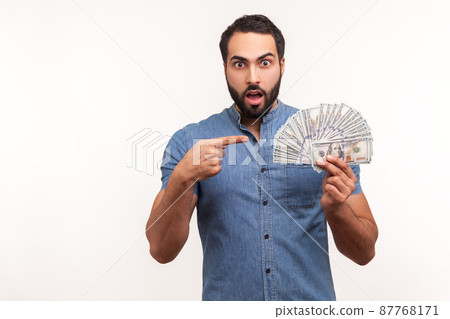 Surprised bearded man pointing at fan of dollar cash in his hand, money exchange, shocked with interest rate. Indoor studio shot isolated on white background Surprised bearded man pointing at fan of dollar cash in his hand, money exchange, shocked with interest rate. Indoor studio shot isolated on white background 87768171