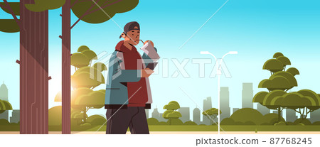 man drinking coffee with straw and using smartphone while walking in urban park social media communication digital addiction man drinking coffee with straw and using smartphone while walking in urban park social media communication digital addiction 87768245