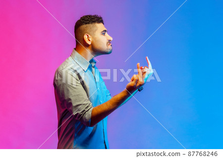Side view of aggressive man in shirt showing middle finger and asking to get off expressing negativity, disrespectful behaviour. Indoor studio shot isolated on colorful neon light background. 87768246