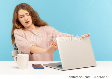 Forbidden content. Frightened woman employee closing laptop and keeping hand in stop gesture to cover shameful post on internet, troubles with computer. indoor studio shot isolated on blue background 87768448