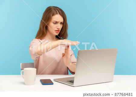 Tired upset woman employee showing time out gesture and looking at laptop screen, talking on video call, asking pause, break of online communication. indoor studio shot isolated on blue background Tired upset woman employee showing time out gesture and looking at laptop screen, talking on video call, asking pause, break of online communication. indoor studio shot isolated on blue background 87768481