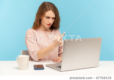 Furious rude young woman employee showing middle finger to laptop screen, aggressively communicating on video call, expressing disrespect and hate. indoor studio shot isolated on blue background 87768529