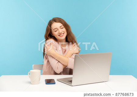 I love myself. Adorable happy woman employee at workplace embracing herself with pleasure expression, feeling proud and satisfied, positive self-esteem. indoor studio shot isolated on blue background I love myself. Adorable happy woman employee at workplace embracing herself with pleasure expression, feeling proud and satisfied, positive self-esteem. indoor studio shot isolated on blue background 87768673