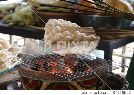 A indigenous rice cracker on bamboo is grilling over stove. A indigenous rice cracker on bamboo is grilling over stove. 87768697