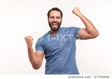 Euphoric thrilled man with beard screaming hurray raising hands up, celebrating his triumph and victory, extremely satisfied with success. Indoor studio shot isolated on white background Euphoric thrilled man with beard screaming hurray raising hands up, celebrating his triumph and victory, extremely satisfied with success. Indoor studio shot isolated on white background 87768698