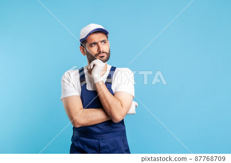 Pensive confused handyman in overalls holding chin, thinking over decision, having suspicion and doubting choice. Profession of service industry, courier delivery, housekeeping maintenance. isolated 87768709