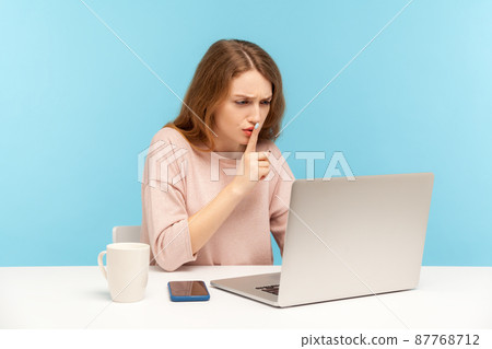 Please, keep secret. Woman employee at workplace shushing with silence gesture, talking on video call, online communication via laptop at home office. indoor studio shot isolated on blue background 87768712