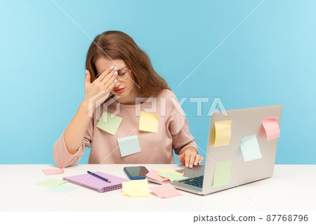 Exhausted fatigued overworked woman employee in glasses covered with sticky notes, touching head thinking desperate, suffering headache of work overload. indoor studio shot isolated on blue background 87768796