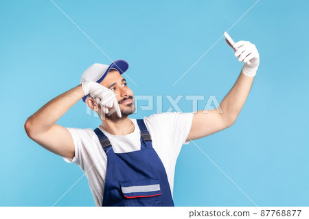 Worker in overalls and gloves pointing finger down while talking on video call, communicating online with client using mobile phone, accepting order as delivery, repair and maintenance services 87768877