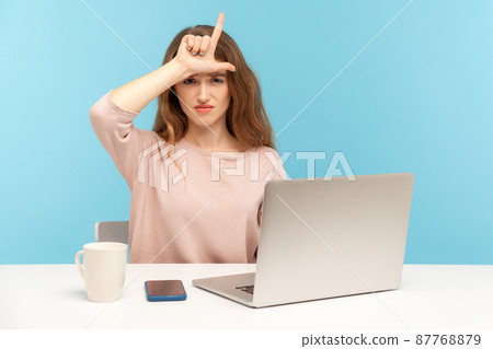 Lost job, unemployment. Depressed young woman employee sitting at workplace with laptop and showing loser gesture, desperate about unlucky dismissal. indoor studio shot isolated on blue background Lost job, unemployment. Depressed young woman employee sitting at workplace with laptop and showing loser gesture, desperate about unlucky dismissal. indoor studio shot isolated on blue background 87768879