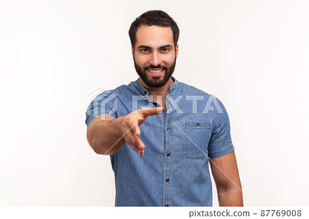 Smiling friendly man with beard in blue shirt holding hand for handshake, happy to make agreement, successful partnership. Indoor studio shot isolated on white background 87769008