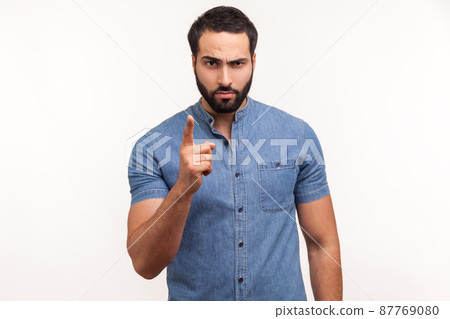 Serious bossy man with beard in blue shirt warning with finger, scolding, strictly looking at camera. Indoor studio shot isolated on white background 87769080