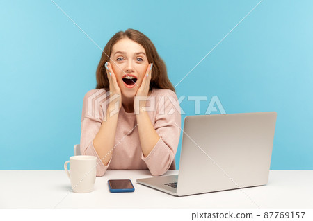 Wow, unbelievable. Surprised astonished young woman employee sitting at workplace with open mouth, shouting in amazement, shocked by unexpected news. indoor studio shot isolated on blue background Wow, unbelievable. Surprised astonished young woman employee sitting at workplace with open mouth, shouting in amazement, shocked by unexpected news. indoor studio shot isolated on blue background 87769157