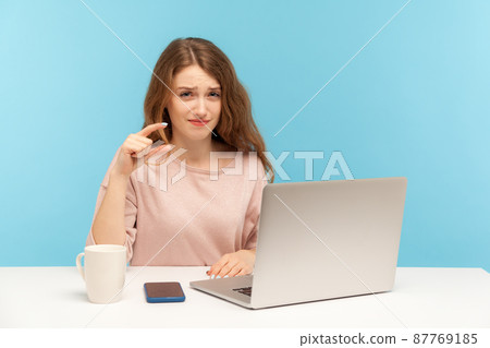 Too small amount, low rating. Disappointed upset woman employee sitting at workplace with laptop and showing a little bit gesture, measuring minimum. indoor studio shot isolated on blue background 87769185