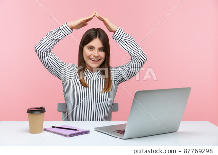 Positive smiling business woman raising hands above head showing roof sitting at workplace, freelancer, working in home office, teleworking. Indoor studio shot isolated on pink background Positive smiling business woman raising hands above head showing roof sitting at workplace, freelancer, working in home office, teleworking. Indoor studio shot isolated on pink background 87769298