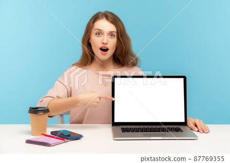 Amazed astonished woman, office employee, sitting at workplace and pointing empty laptop screen, mock up display for advertisement, commercial website. indoor studio shot isolated on blue background 87769355