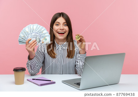 Surprised woman office worker holding hundreds dollars and bitcoin crypto currency, looking at camera with astonishment, shocked with exchange rate. Indoor studio shot isolated on pink background Surprised woman office worker holding hundreds dollars and bitcoin crypto currency, looking at camera with astonishment, shocked with exchange rate. Indoor studio shot isolated on pink background 87769438