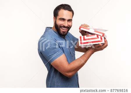 Happy smiling man holding unpacked gift box, pleased satisfied with holiday present, dreams comes true, pleasant surprises and bonuses. Indoor studio shot isolated on white background 87769816