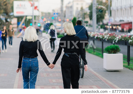 Two young females walking smiling embracing and kissing outdoor in the city Two young females walking smiling embracing and kissing outdoor in the city 87773576