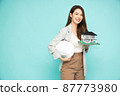 Home inspector Asian woman or engineer holding a white helmet and single-family home or detached house model isolated on green background 87773980