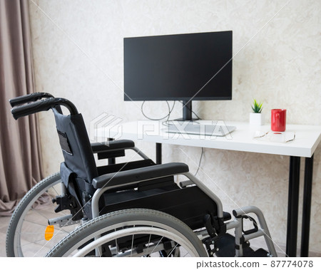 Workplace for a disabled person. Wheelchair at the table with a computer.  87774078