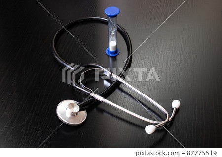 Stethoscope and hourglass on a wooden table 87775519