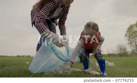 Volunteer happy family collects plastic trash in bags, teamwork, little girl helps adults in the fight for environmental protection, eco, kid with mom clears land from landfill, charity work Volunteer happy family collects plastic trash in bags, teamwork, little girl helps adults in the fight for environmental protection, eco, kid with mom clears land from landfill, charity work 87776253