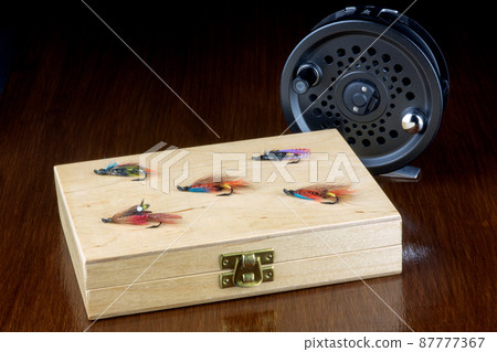 Wooden Fishing Fly Box with Flies and Fly Reel on a Polished Table Top Wooden Fishing Fly Box with Flies and Fly Reel on a Polished Table Top 87777367