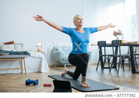 elderly woman doing exercises with an online trainer in her living room. 87777392