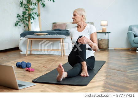 elderly woman performing pilates gymnastics online in her living room. elderly woman performing pilates gymnastics online in her living room. 87777421
