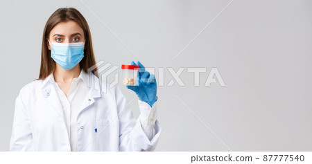 Covid-19, preventing virus, healthcare workers and quarantine concept. Doctor in scrubs and medical mask, showing container with pills, recommend vitamins or antibiotics 87777540