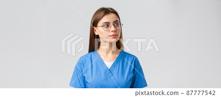 Healthcare workers, medicine, insurance and covid-19 pandemic concept. Thoughtful pretty professional female nurse, doctor in glasses and scrubs, looking right curious, thinking, observe something 87777542