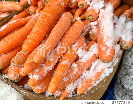 pile of fresh and ripe carrots covered with snow in open market or grocery 87777869