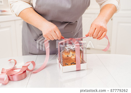 a female cook packs a Kraffin, easter cake in a box with satin ribbon a female cook packs a Kraffin, easter cake in a box with satin ribbon 87779262