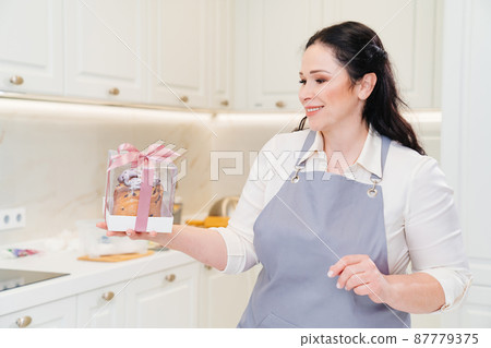 female cook with Kraffin, easter cake in a box with satin ribbon in the kitchen. female cook with Kraffin, easter cake in a box with satin ribbon in the kitchen. 87779375