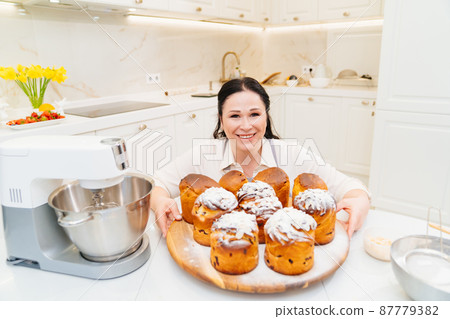 female cook with Kraffins, easter cakes and Panettones in the kitchen. female cook with Kraffins, easter cakes and Panettones in the kitchen. 87779382
