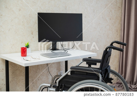 Workplace for a disabled person. Wheelchair at the table with a computer.  87780183