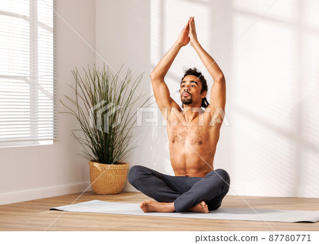 Relaxed black man with hands raised up meditating near potted plant Relaxed black man with hands raised up meditating near potted plant 87780771