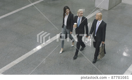 high angle view of three corporate executives talking while walking across lobby of modern office building 87781081