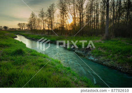 A small river and sunset behind the trees A small river and sunset behind the trees 87782610